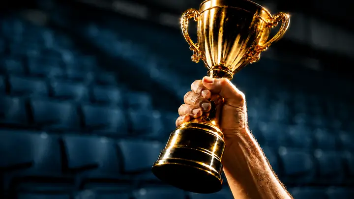 A hand raising a gold championship trophy in a stadium